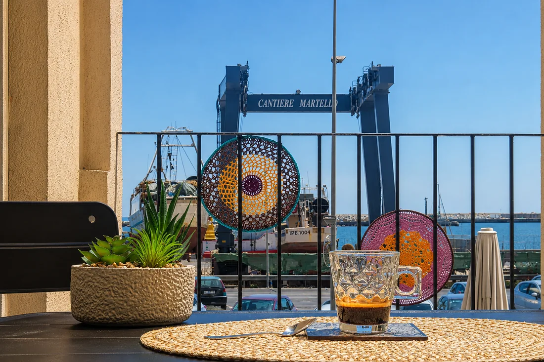 Il caffè sul tavolo del terrazzino, e dietro la ringhiera il porto con i pescherecci e la gru del cantiere